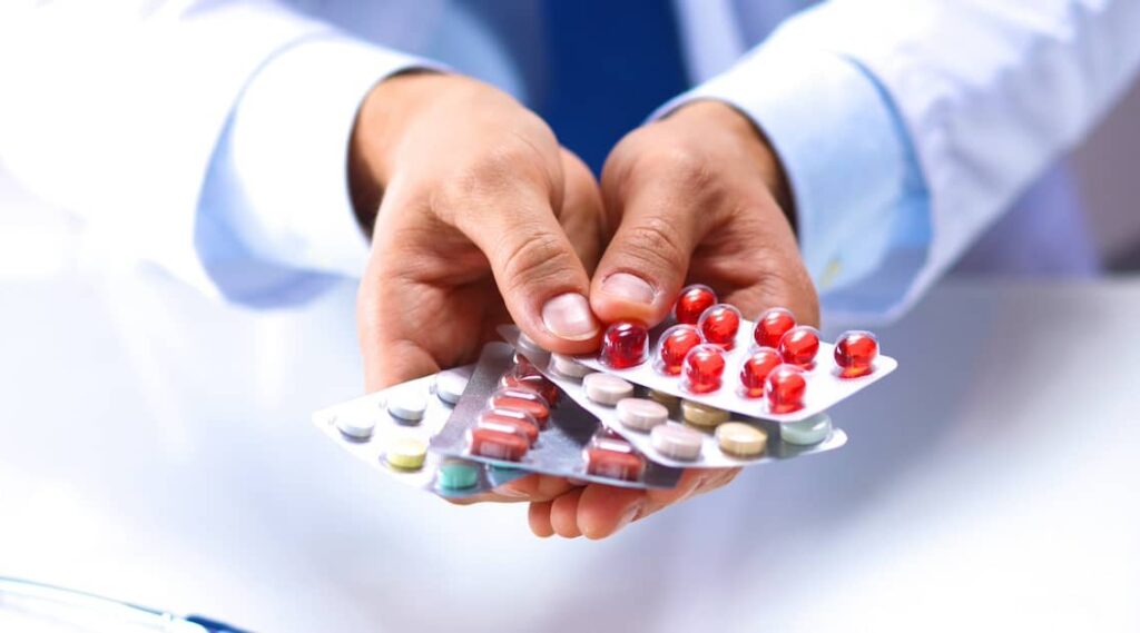 Doctor overprescribing medications, holding multiple pill samples | Henry Carus + Associates