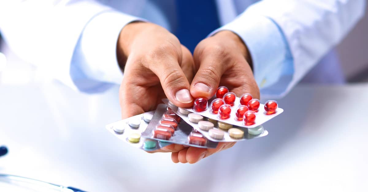 Doctor overprescribing medications, holding multiple pill samples | Henry Carus + Associates