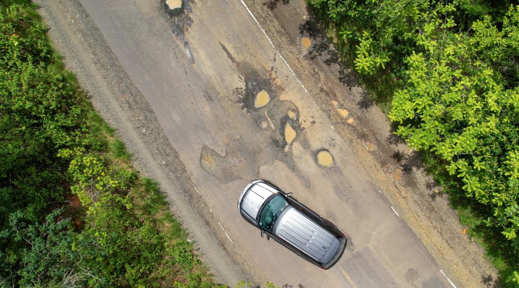 Large potholes on a wet Victorian highway with a car driving to avoid