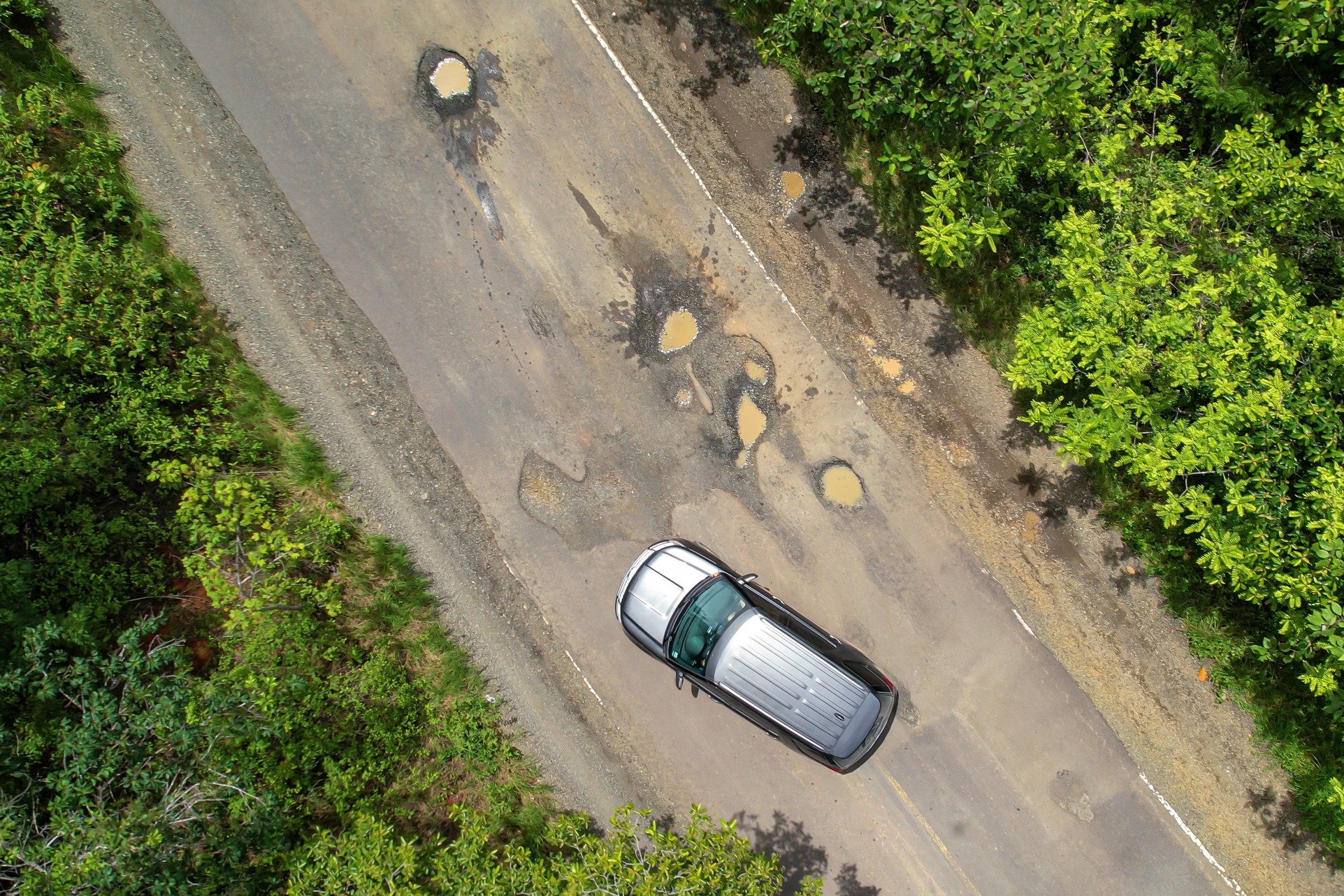 Large potholes on a wet Victorian highway with a car driving to avoid